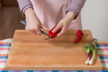 Close up of hands peeling and cutting red peppers on a wooden board. Healthy food preparation concept