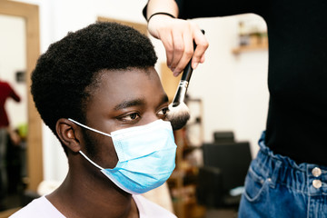 hairdresser making up a black African-American man with a mask brush