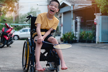 Asian special child on wheelchair is playing badminton to strengthen muscles in the house, Lifestyle of disabled child,Life in the education age of children, Happy disability kid stay at home concept.