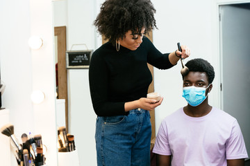 black african american hairdresser making up a black african american man with a brush both with masks reflected in the mirror