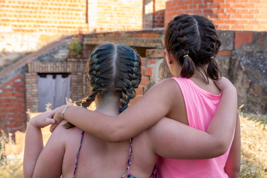 Blonde and brunette teenagers with braids in their hair hugging. 