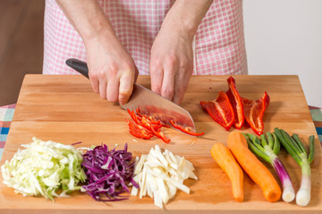 Close up of hands chopping red peppers on a wooden board. Healthy food preparation concept