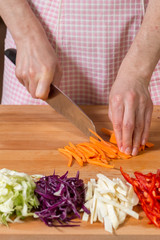 Close up of hands chopping carrots on a wooden board...Healthy food preparation concept