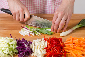 Close up of hands chopping scallions on a wooden board. Healthy food preparation concept