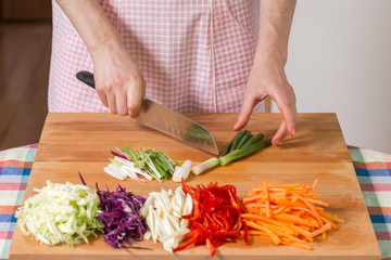 Close up of hands chopping scallions on a wooden board. Healthy food preparation concept