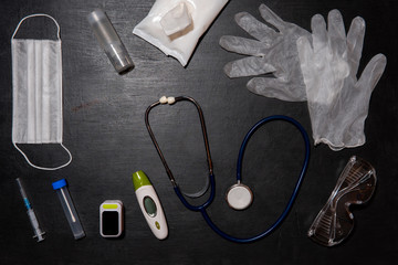 Doctor’s equipment-stethoscope, thermometer, oximeter, test tube, medical mask, disposable gloves, antiseptic gel, antibacterial wipes and syringe on black background