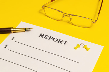 The report form on the yellow office desk with glasses and pen