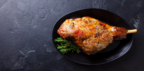 Roasted lamb leg on a plate. Black background. Copy space. Top view.