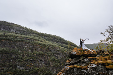 Portrait of a wedding couple standing on a rock. The newlyweds cling to each other, the bride waves her hand