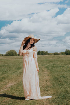 Stylish girl in linen dress and hat walking among herbs and wildflowers in sunny field in mountains. Boho woman