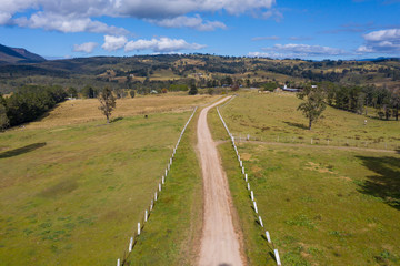 Aerial view of a dirt road with white fence post markers in a green agricultural field