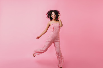 Bright, brave girl in great mood jumping in studio. Photo taken on pink background of cute model in stylish summer outfit