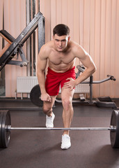 Fototapeta na wymiar Young man flexing muscles with barbell in gym.