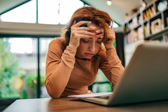 Close-up portrait of a stressed woman looking at received letter, holding head in hands.