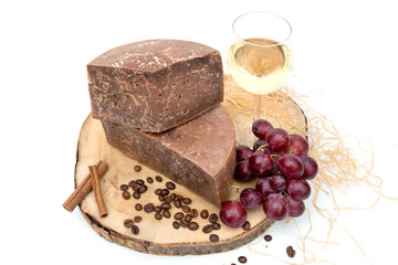 
tasty hard seasoned chocolate cheese natural product on a wooden board decorated with cinnamon, ouch and grapes, a beautiful picture with cheese, close-up, white background, top view