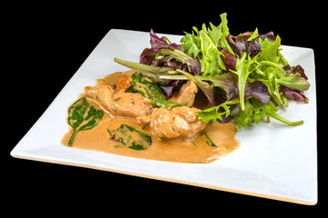 Gourmet chicken legs with lettuce and sauce on a white plate, isolated on black background.