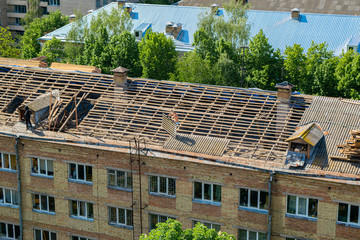 Workers repair and replace roofing on an old red brick building. Spring construction work. Repair and maintenance of city buildings in proper form.