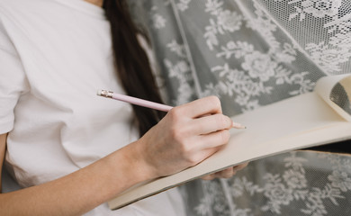 Woman draws in a sketchbook at home near the window, creativity. Drawing training.