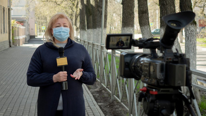 A female journalist in a protective medical mask is reporting in a deserted city.