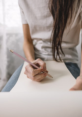 Woman artist draws in a sketchbook at home near the window, sitting on a chair in comfort and coziness, creativity. Drawing training.