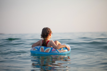 young girl in glasses swims in the water on an inflatable donut in the hot sunny summer
