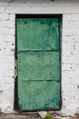 Old metal and wood door painted with green paint against the background of an old white tiles