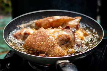 A close-up shot of streaky pork cooking in a frying pan has hot oil and it looks delicious.