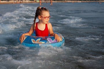 Obraz premium young girl in glasses plays in the water on an inflatable donut in a hot sunny summer