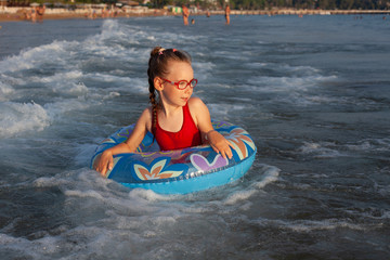 Obraz premium young girl in glasses plays in the water on an inflatable donut in a hot sunny summer