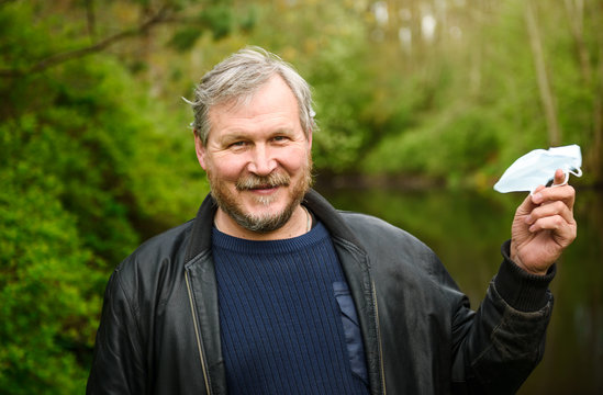 A happy middle-aged man removes a medical mask from his face in a spring Park. Over the coronavirus. End of the pandemic, epidemic, and quarantine.