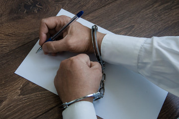 Male hands in handcuffs with a pen and a sheet of white paper. Concept the detainee writes a...
