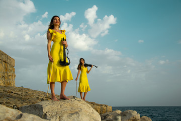 Two beautiful twin sisters violinists in yellow concert dresses are playing electric violins on...