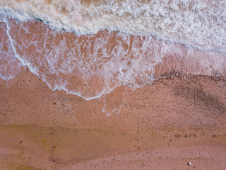 Top down view of waves breaking in the sand, flying over tropical sandy beach and waves