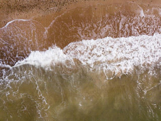 Top down view of waves breaking in the sand, flying over tropical sandy beach and waves