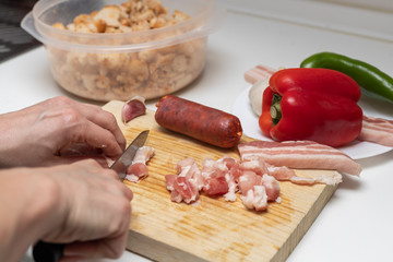 Hands cutting bacon. Extremadura crumbs, traditional home cooking with bacon, chorizo, garlic, breadcrumbs, red and green peppers plus paprika