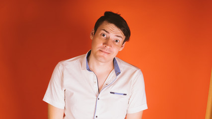 A young handsome man in a white shirt is offended by something or someone on an orange background.