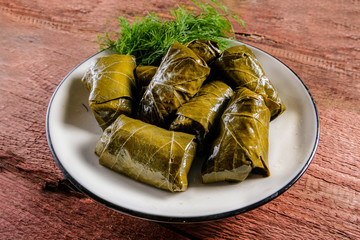 Traditional Georgian and Greek, Turkish dolma in grape leaves with sour cream sauce and herbs on a table made of red wooden boards.