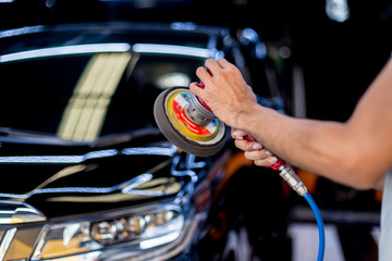 The worker polishes a car with the electric tool.