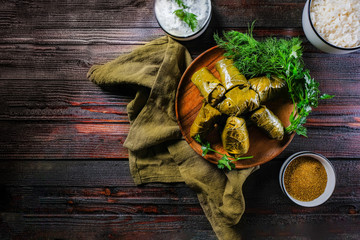 Homemade dolma on a dark wooden background with herbs, spices and sour cream sauce. Copy space