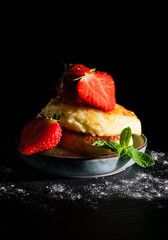 still life cheesecakes with strawberries and a leaf of mint, sprinkled with honey on a black background