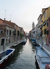 Narrow clear canal view in Venice with boats