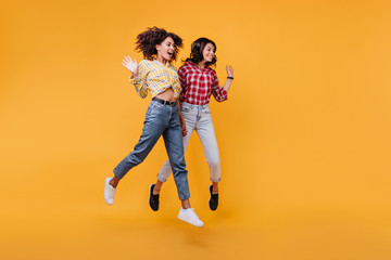Pretty girls waving their hands in greeting. Photo indoors of young women in plaid shirts sincerely...