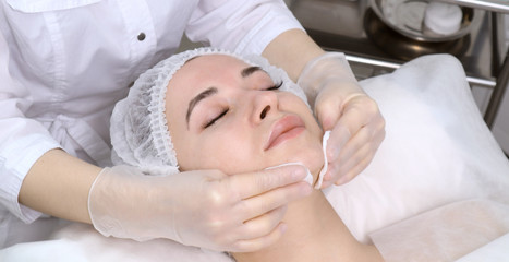 Naklejka premium Beautician makes the cleansing procedure a young beautiful girl patient. The concept of skin care face and body
