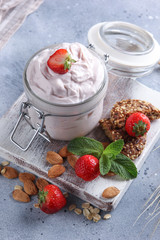 Fermented milk product. Healthy strawberry yogurt in a transparent jar on a white wooden board with fresh berries, mint, nuts and cookies on a light grey background. Background image, copy space