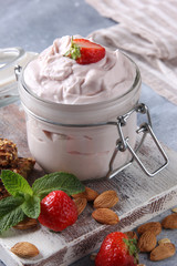 Fermented milk product. Healthy strawberry yogurt in a transparent jar on a white wooden board with fresh berries, mint, nuts and cookies on a light grey background. Background image, copy space