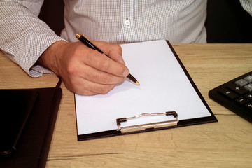 Man's hand holds a pen. On the table are a calculator, diary, telephone. Accounting, finance, banking concept.