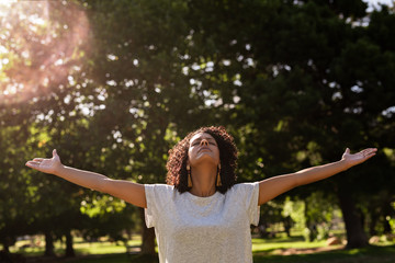 Woman standing in a park with her arms raised upwards