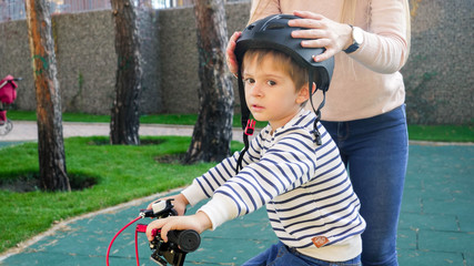 Young caring mother puts on protective helmet on her little son before riding bicycle