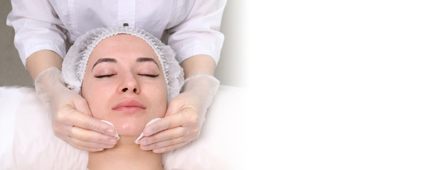 Beautician makes the cleansing procedure a young beautiful girl patient. The concept of skin care...