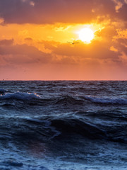 Waves of a sea at sunrise with colourful clouds in background. Vertical view